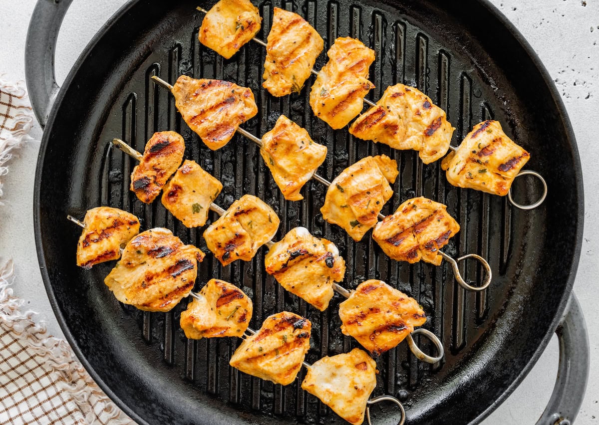 Grilled chicken skewers with char marks cooking on a grill pan.