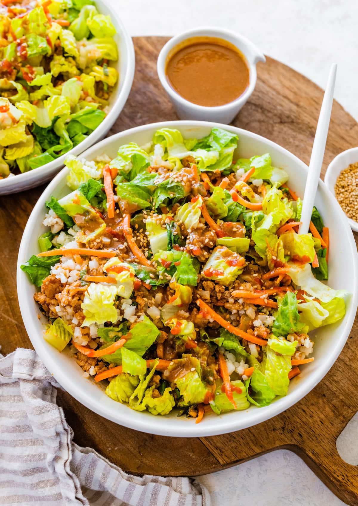Chopped salad version of chicken lettuce wrap bowl with lettuce, cauliflower rice, carrots, and peanut sauce.