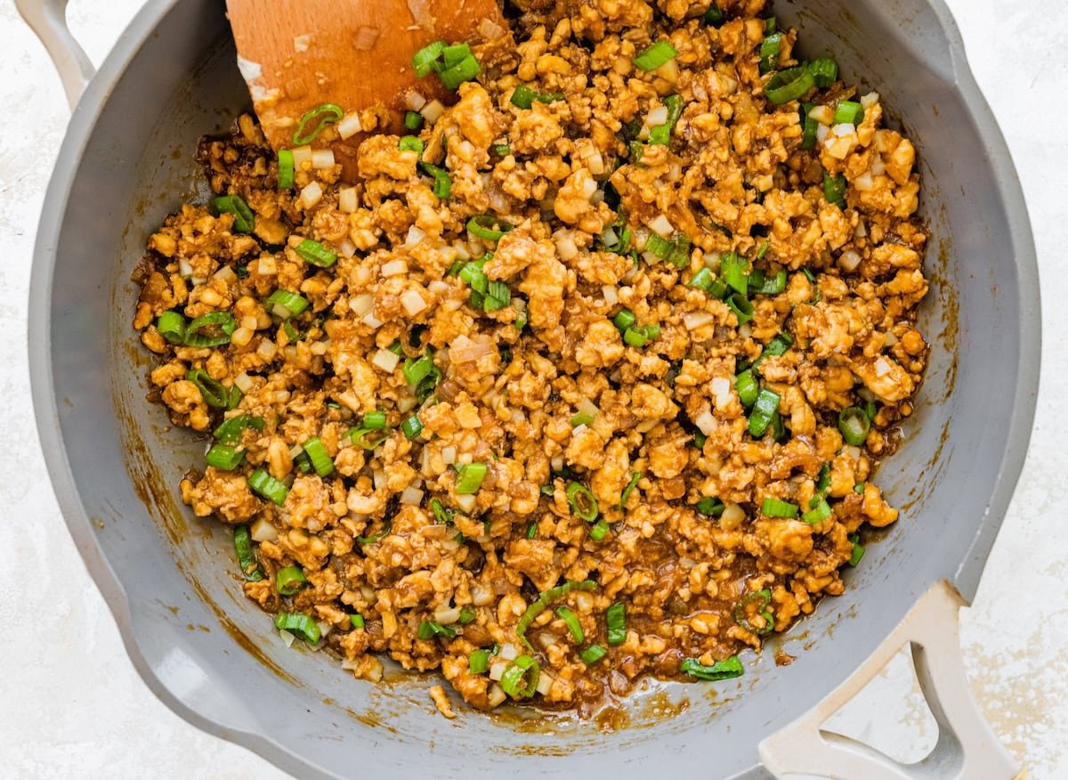 Skillet filled with cooked ground chicken and chopped green onions for lettuce wrap bowls.
