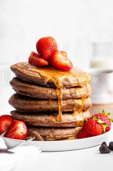 Stack of fluffy chocolate protein pancakes topped with strawberries and nut butter drizzle.