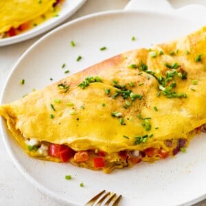 Finished cottage cheese omelette on a plate sprinkled with chives and served with a fork.