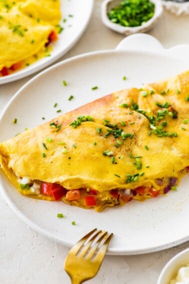 Finished cottage cheese omelette on a plate sprinkled with chives and served with a fork.
