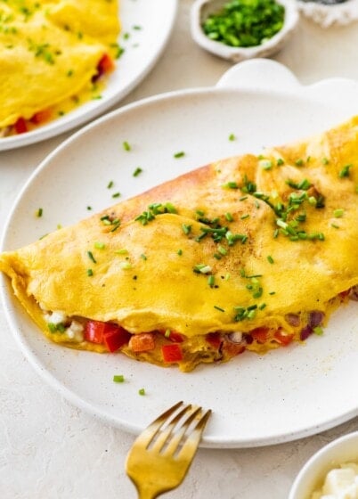 Finished cottage cheese omelette on a plate sprinkled with chives and served with a fork.