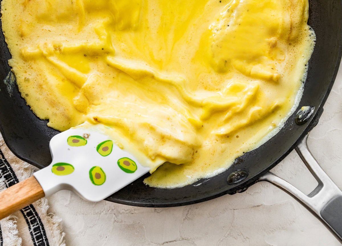 Fluffy blended egg mixture cooking in a skillet while a spatula lifts the edges.