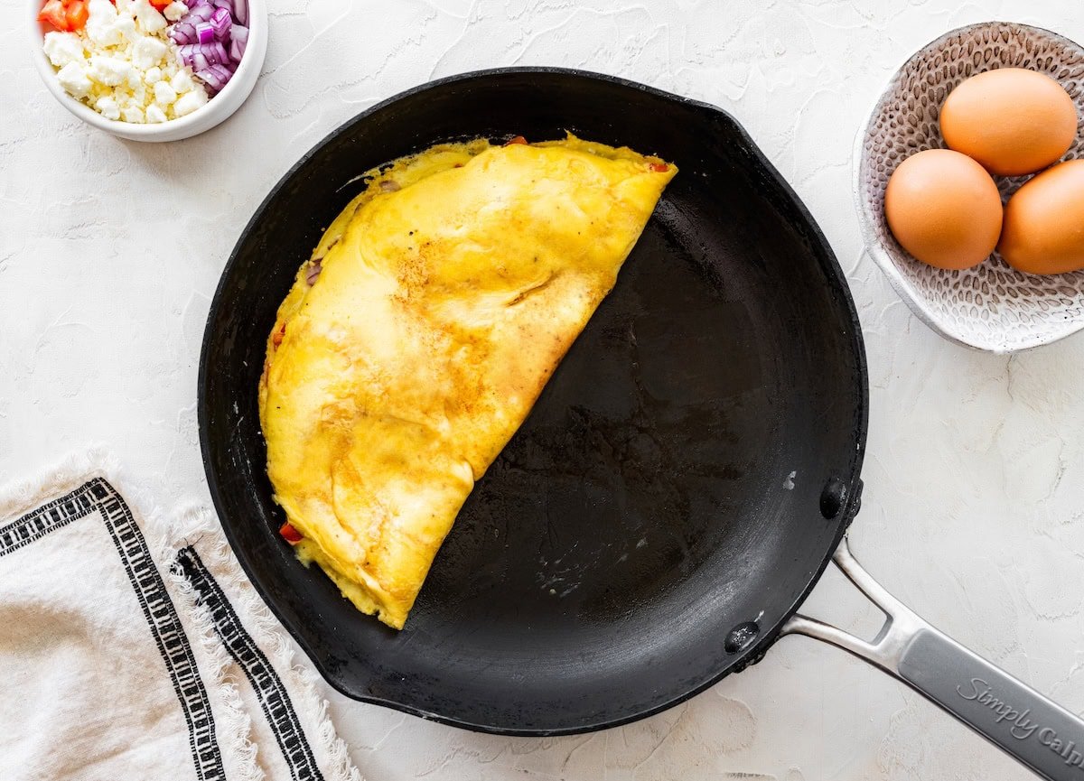 Omelette folded in a skillet with golden edges and peppers tucked inside.