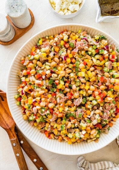Colorful dense bean salad with beans, salami, feta, and veggies in a white serving bowl.
