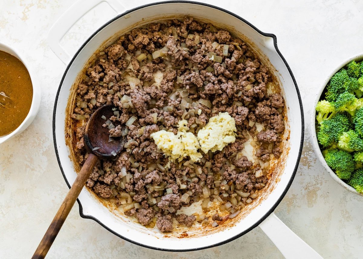 Ground beef being cooked in a white skillet with garlic and onion.