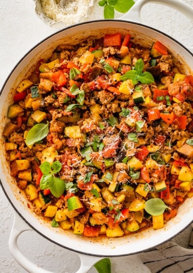 Large skillet filled with cooked ground turkey, vegetables, and tomato sauce topped with basil.