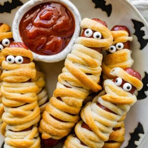 Mummy hot dogs on a Halloween plate served with ketchup for dipping.