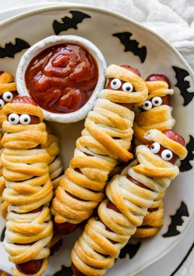 Mummy hot dogs on a Halloween plate served with ketchup for dipping.