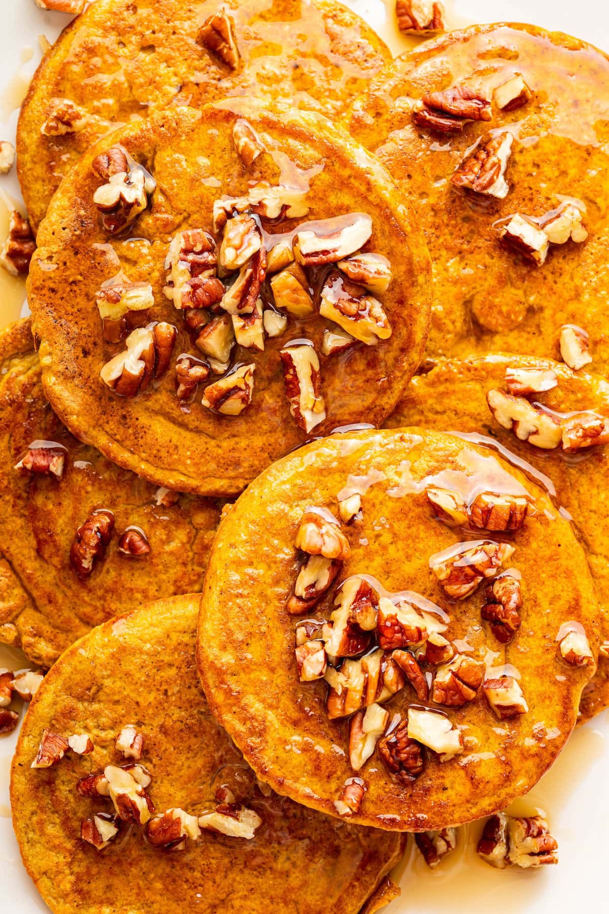 Plate of pumpkin protein pancakes arranged in a circle and topped with chopped pecans and syrup.