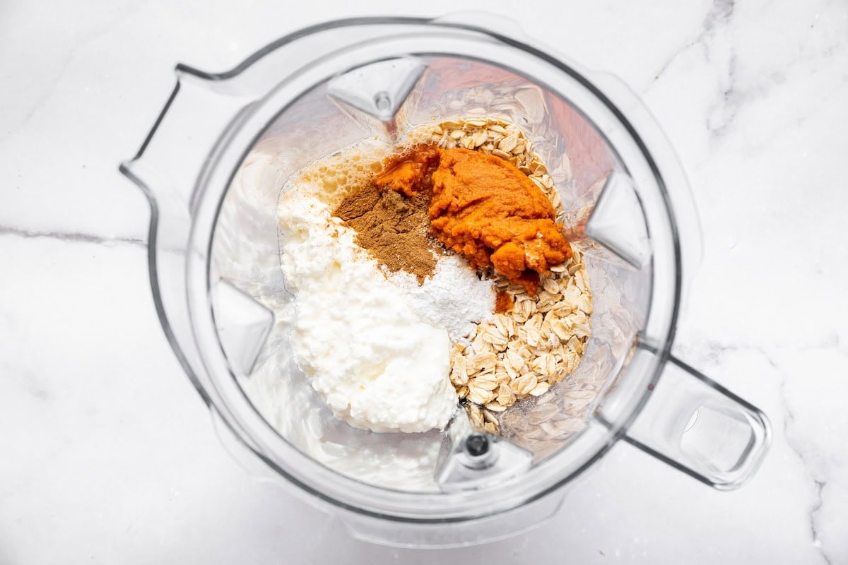 Blender filled with pumpkin purée, oats, cottage cheese, cinnamon, and baking powder.