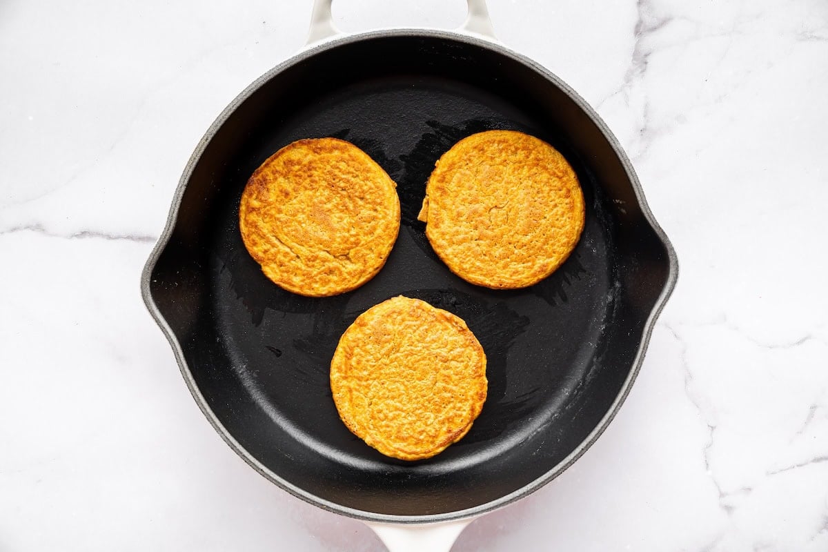 Three pumpkin protein pancakes cooking in a black skillet.