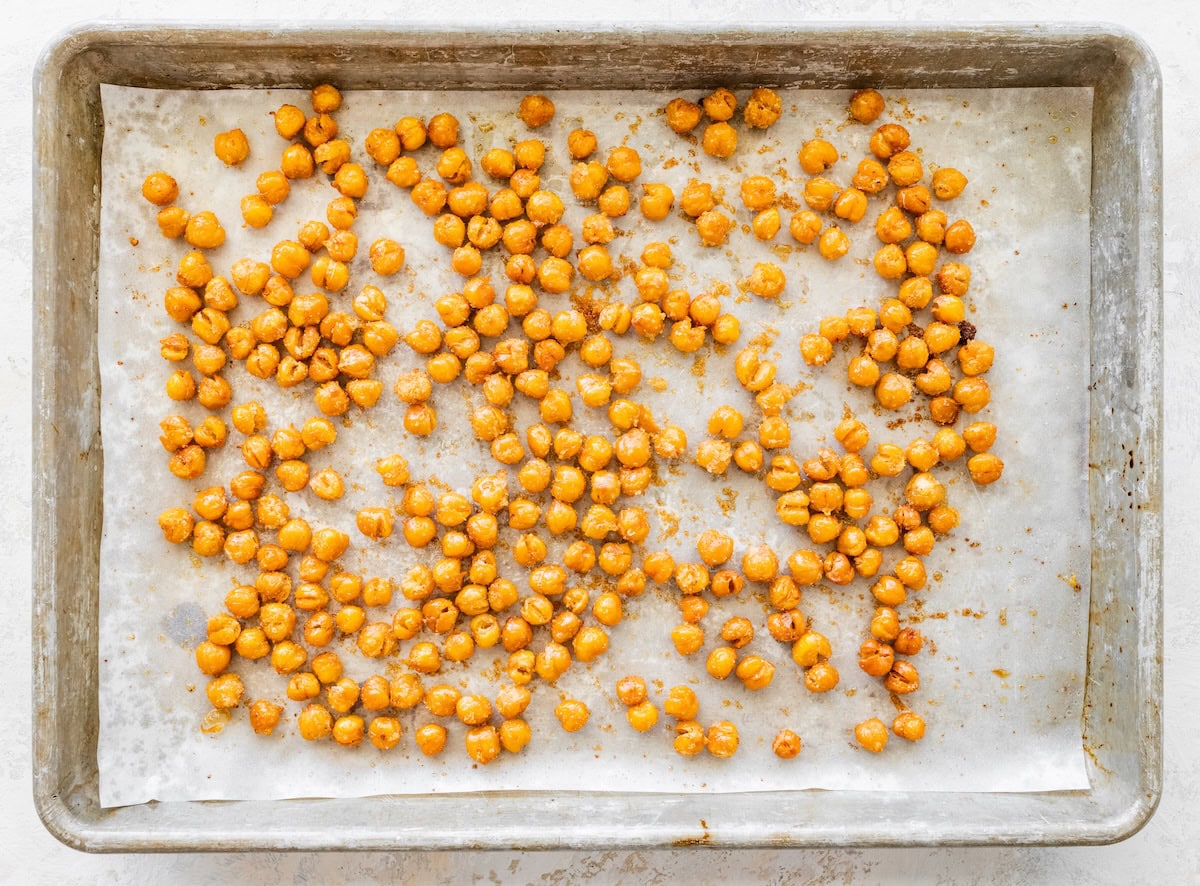 Seasoned chickpeas spread out on a parchment-lined baking sheet after roasting.