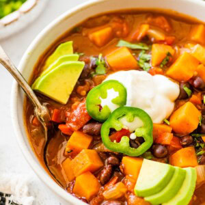 A bowl of sweet potato black bean chili topped with sour cream, jalapeño slices, and avocado.