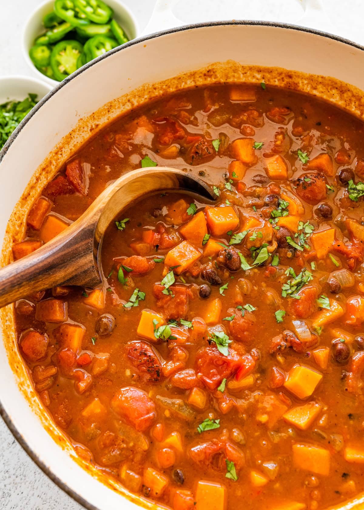 A large pot of sweet potato black bean chili with a wooden serving spoon.