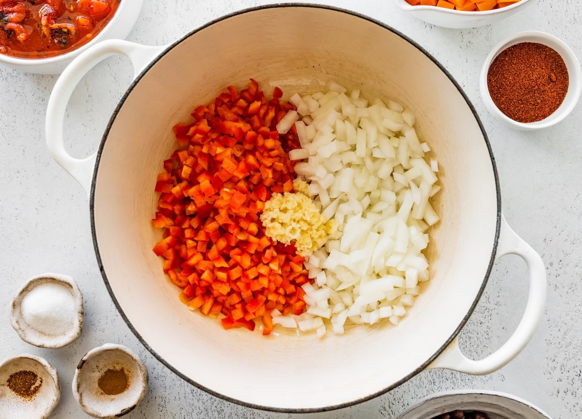 A large pot with diced onion, red bell pepper, and garlic before being sauteed.