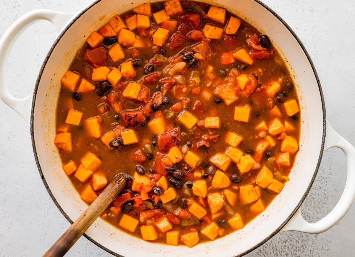 A large pot of sweet potato black bean chili with a wooden serving spoon.