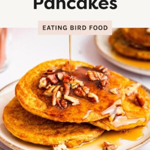 Stack of pumpkin protein pancakes topped with pecans and drizzled with maple syrup on a plate.