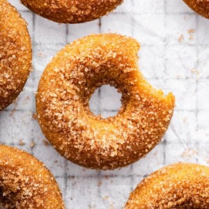 Sugar coated baked apple cider donut on parchment paper on a cooling rack with a bite taken out of it.