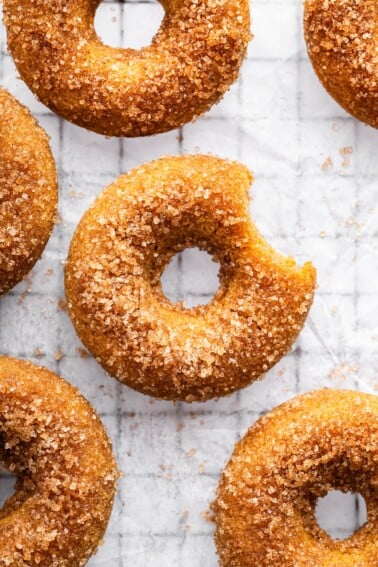 Sugar coated baked apple cider donut on parchment paper on a cooling rack with a bite taken out of it.