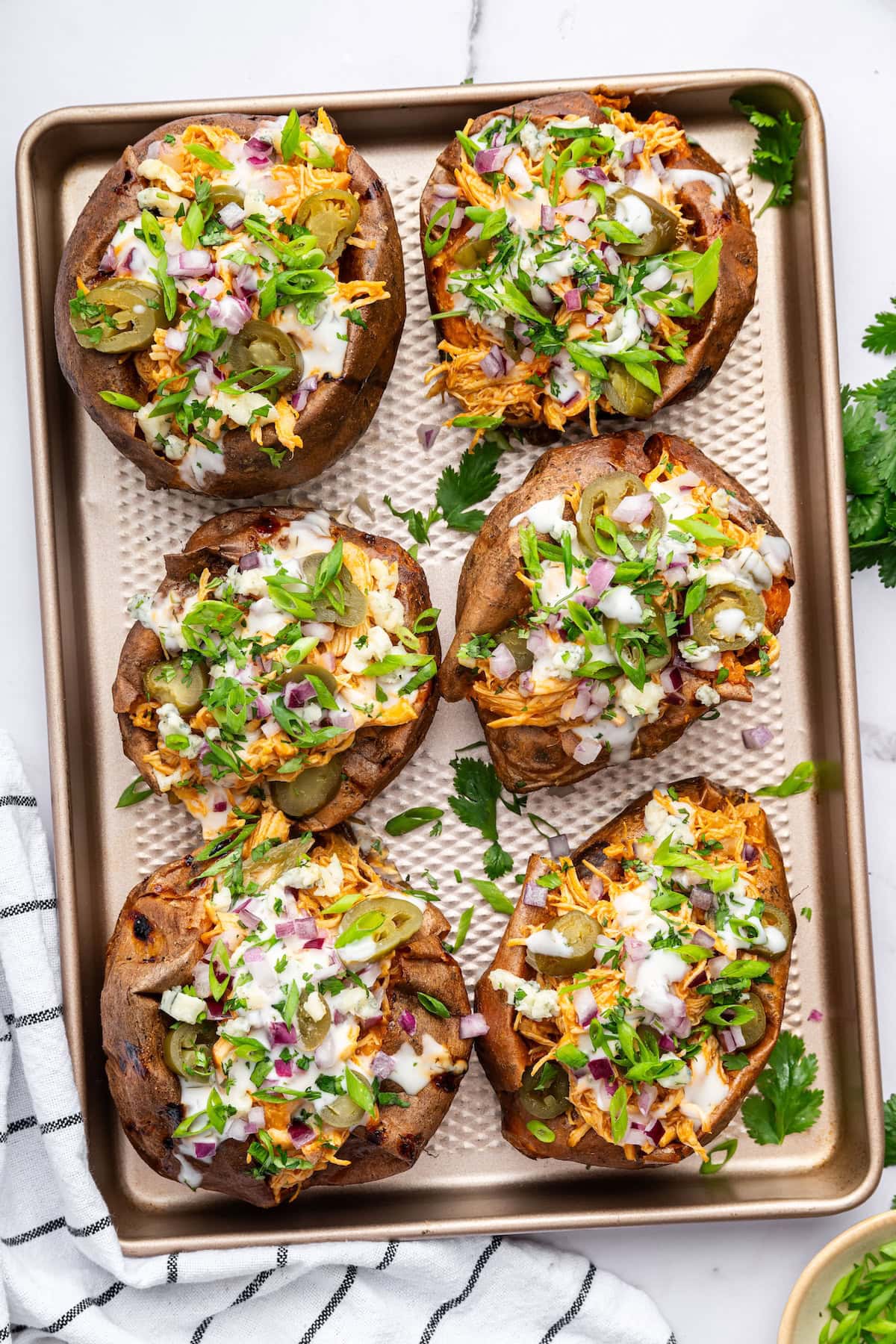 Tray of buffalo chicken stuffed sweet potatoes topped with ranch, jalapeños, onions, and cilantro.