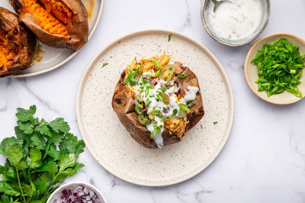 Single buffalo chicken stuffed sweet potato with ranch drizzle on a white speckled plate.