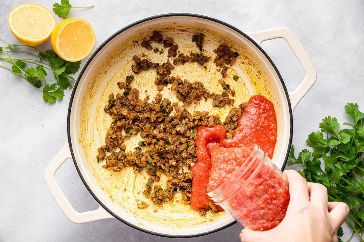 Pouring pureed tomatoes into a pot of sautéed aromatics to make chana masala sauce.