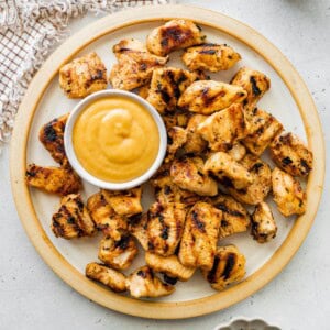 Plate of grilled chicken nuggets served with a small bowl of dipping sauce.