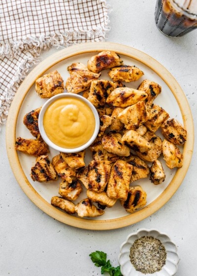 Plate of grilled chicken nuggets served with a small bowl of dipping sauce.