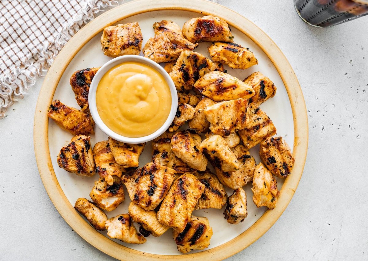 Plate of grilled chicken nuggets served with a small bowl of dipping sauce.