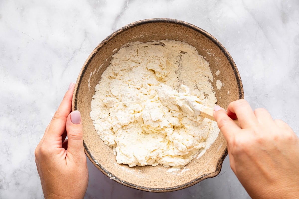 Mixing blended cottage cheese and flour together in a bowl for dough.