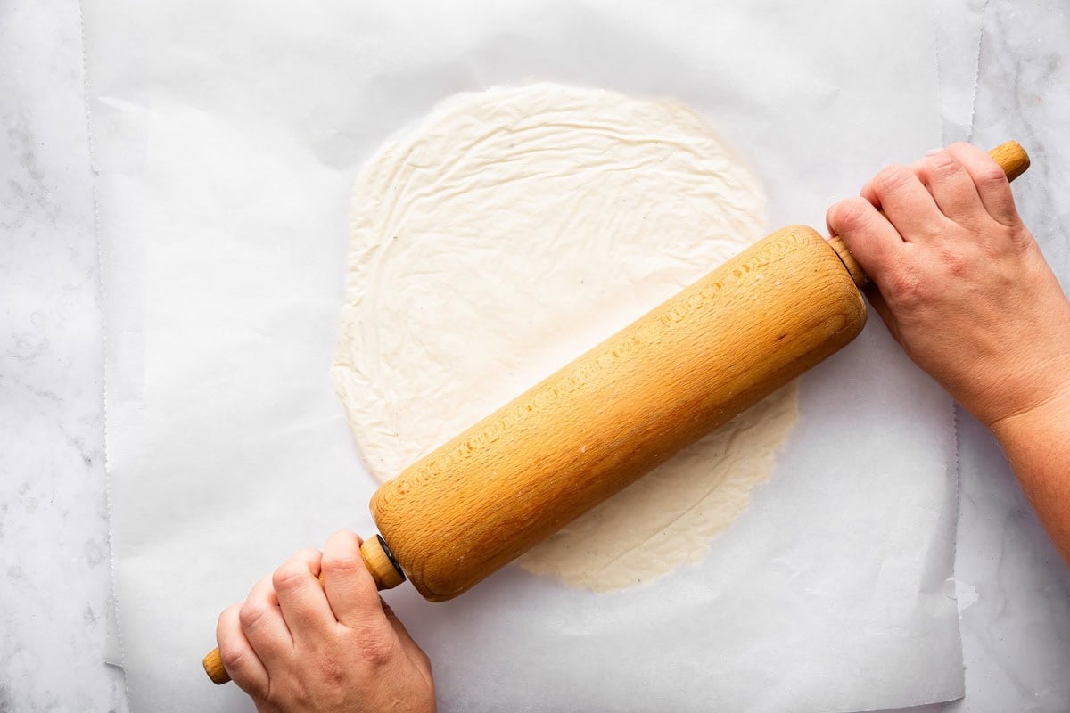 Rolling out cottage cheese pizza dough with a wooden rolling pin.