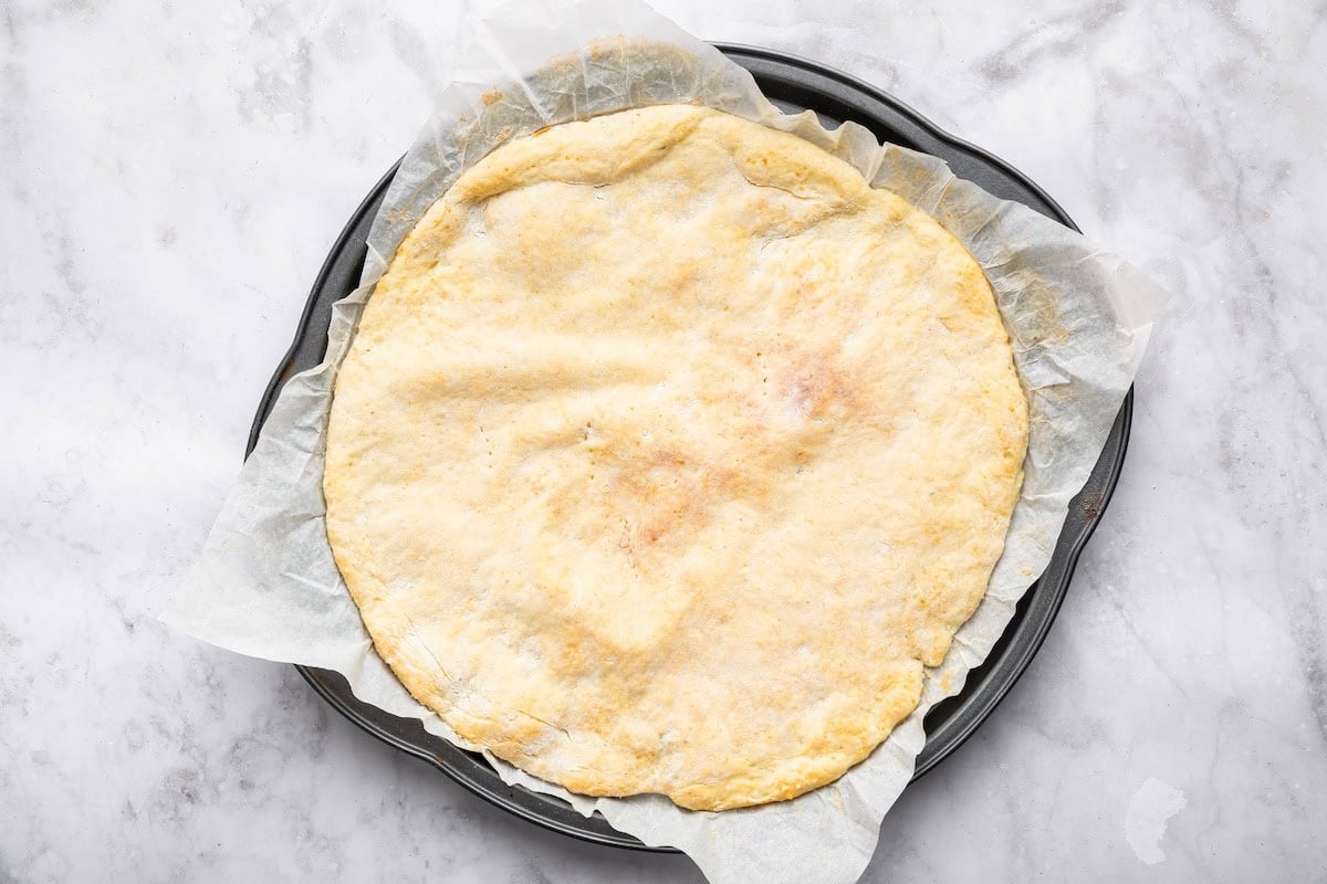 Baked cottage cheese pizza crust in a pizza pan on parchment paper.