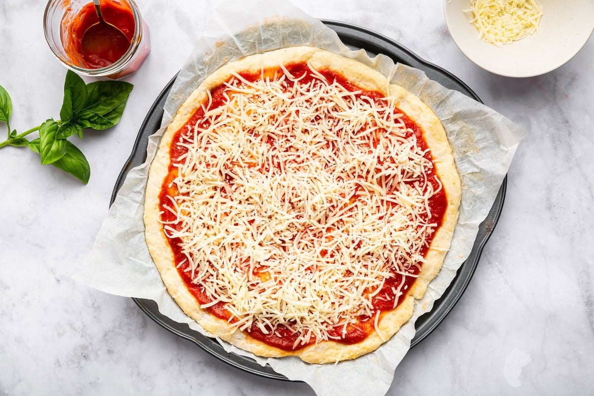 Pizza crust topped with sauce and shredded mozzarella before baking.