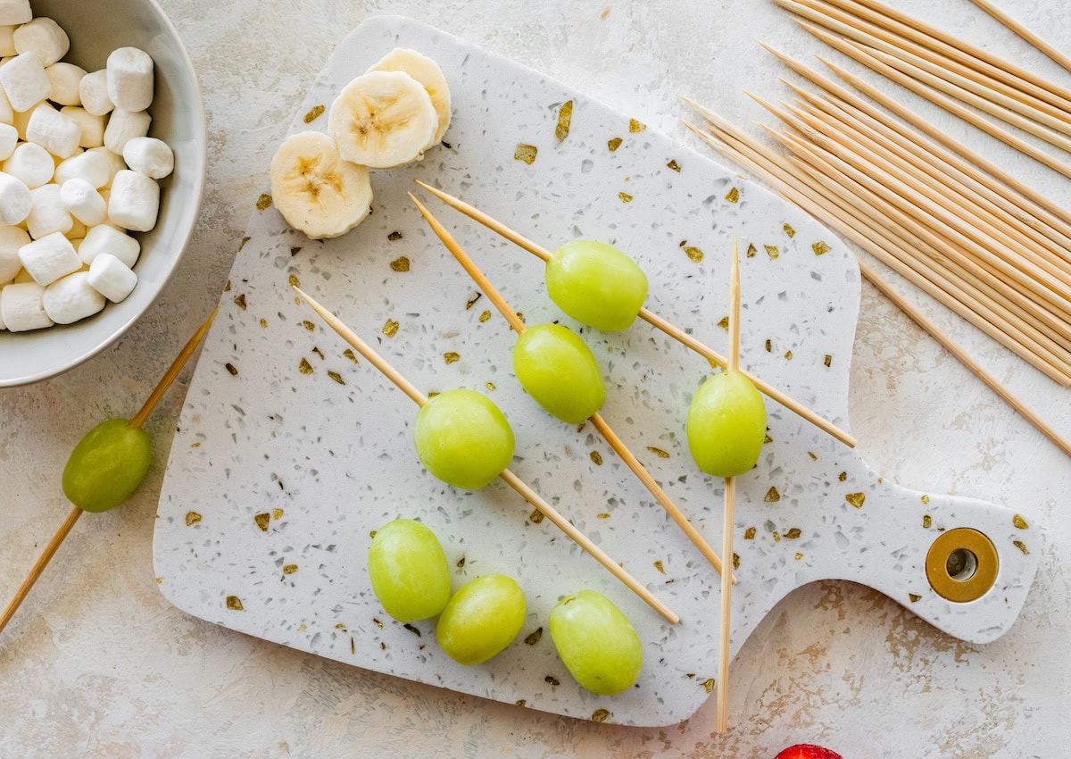Grapes and banana slices on a marble cutting board as the first layer of Grinch kabobs.