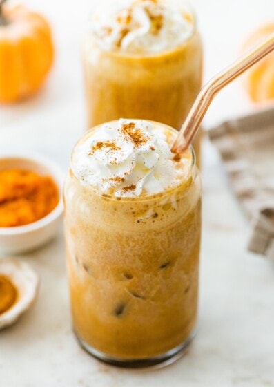 Two iced pumpkin spice lattes with whipped cream and straw.