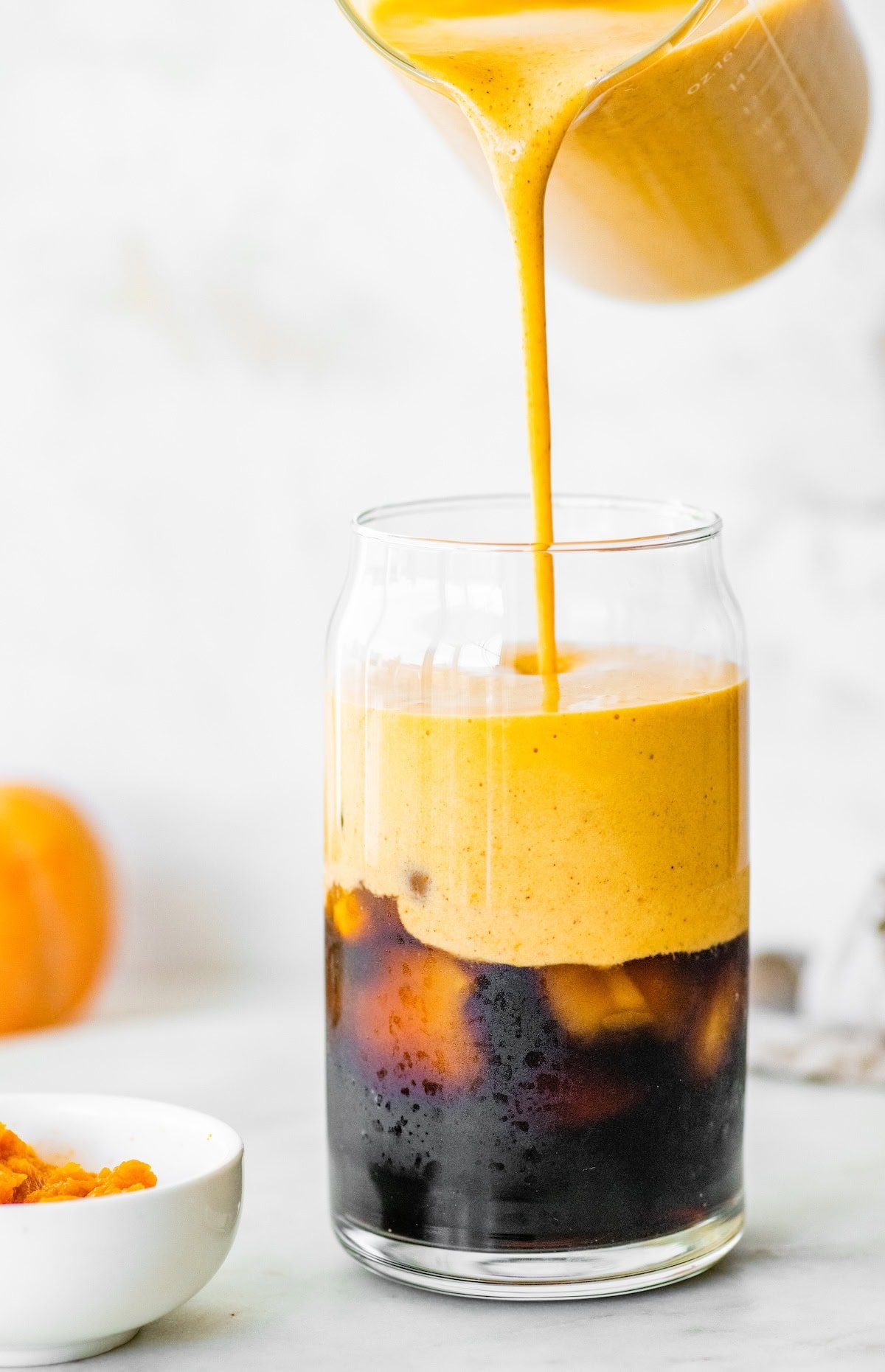 Pumpkin spice latte being poured over iced cold brew coffee.