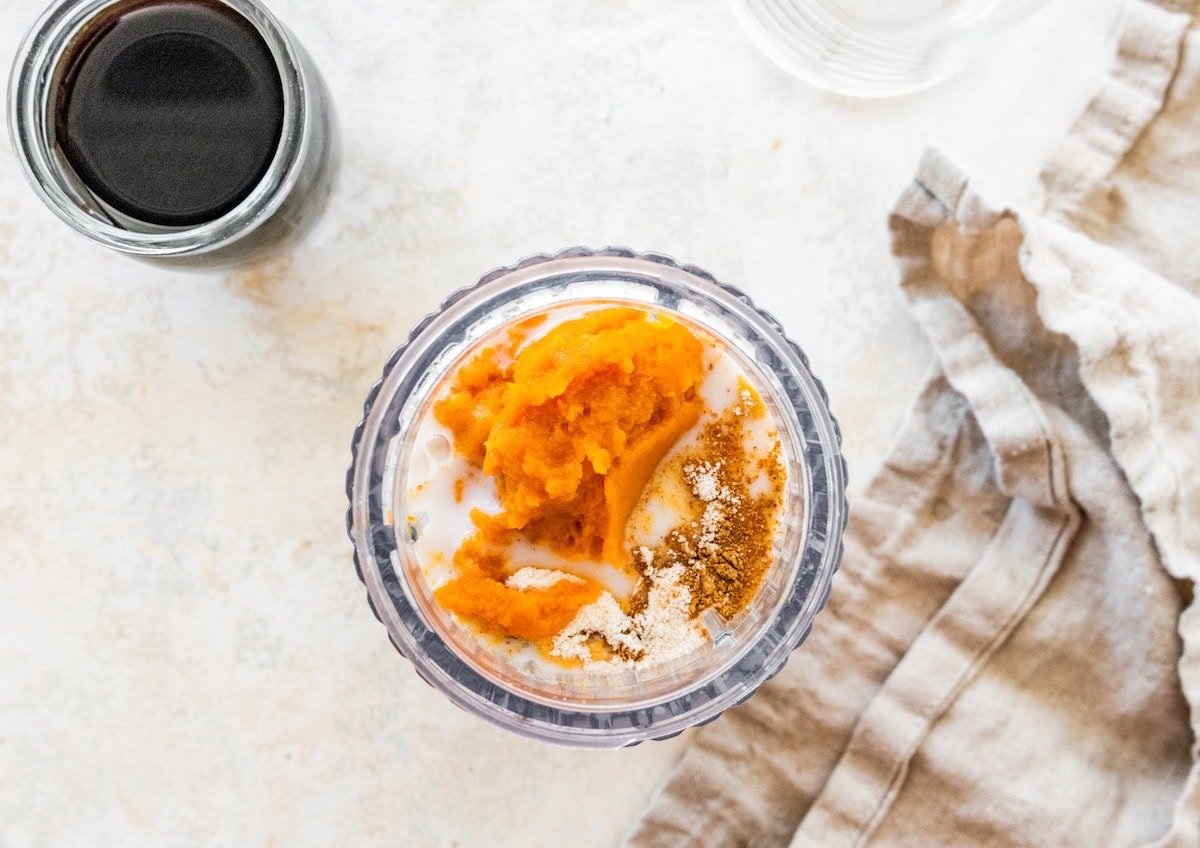 Pumpkin puree and spices in a glass before blending for iced pumpkin spice latte.