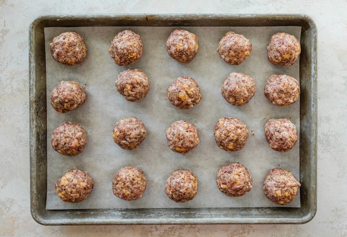 Unbaked sausage balls arranged on a parchment-lined baking sheet, ready to go in the oven.