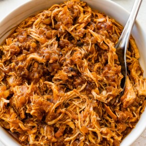 Shredded apple BBQ chicken in a white bowl with a serving spoon.