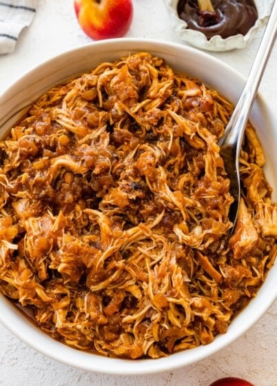 Shredded apple BBQ chicken in a white bowl with a serving spoon.
