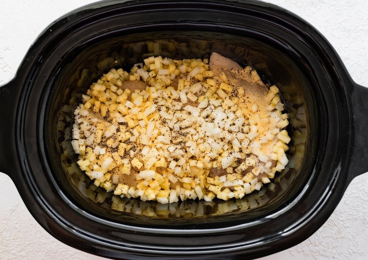 Uncooked chicken, apples and onions in a slow cooker before adding BBQ sauce.