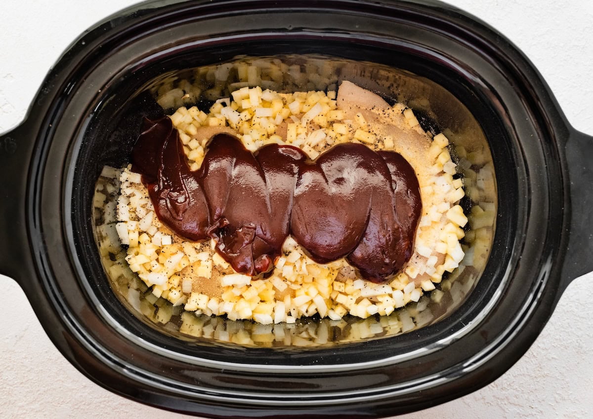Slow cooker filled with chicken, apples, onions and topped with BBQ sauce.