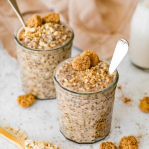 Snickerdoodle overnight oats in two jars topped with cookie crumbles and a spoon in each one.