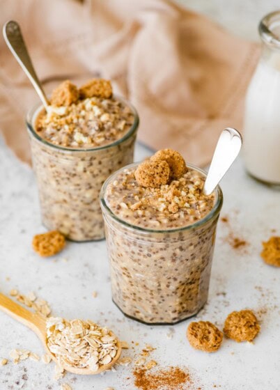 Snickerdoodle overnight oats in two jars topped with cookie crumbles and a spoon in each one.