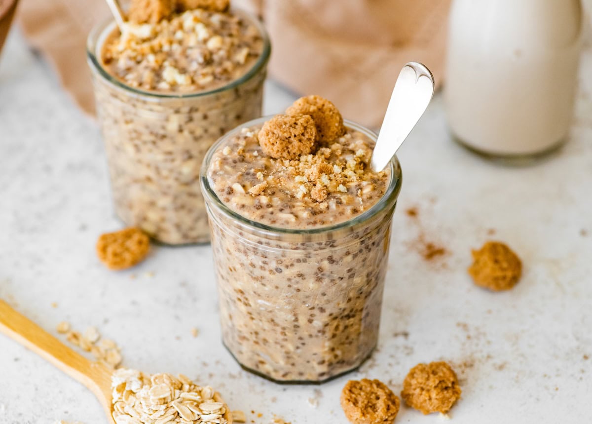 Snickerdoodle Overnight Oats Two jars of snickerdoodle overnight oats with spoons in them topped with cookie crumbles.