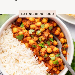 A bowl of chana masala with chickpeas in tomato sauce, garnished with cilantro, served beside white rice.