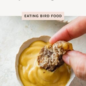 Hand dipping a sausage ball into a small bowl of creamy mustard sauce.