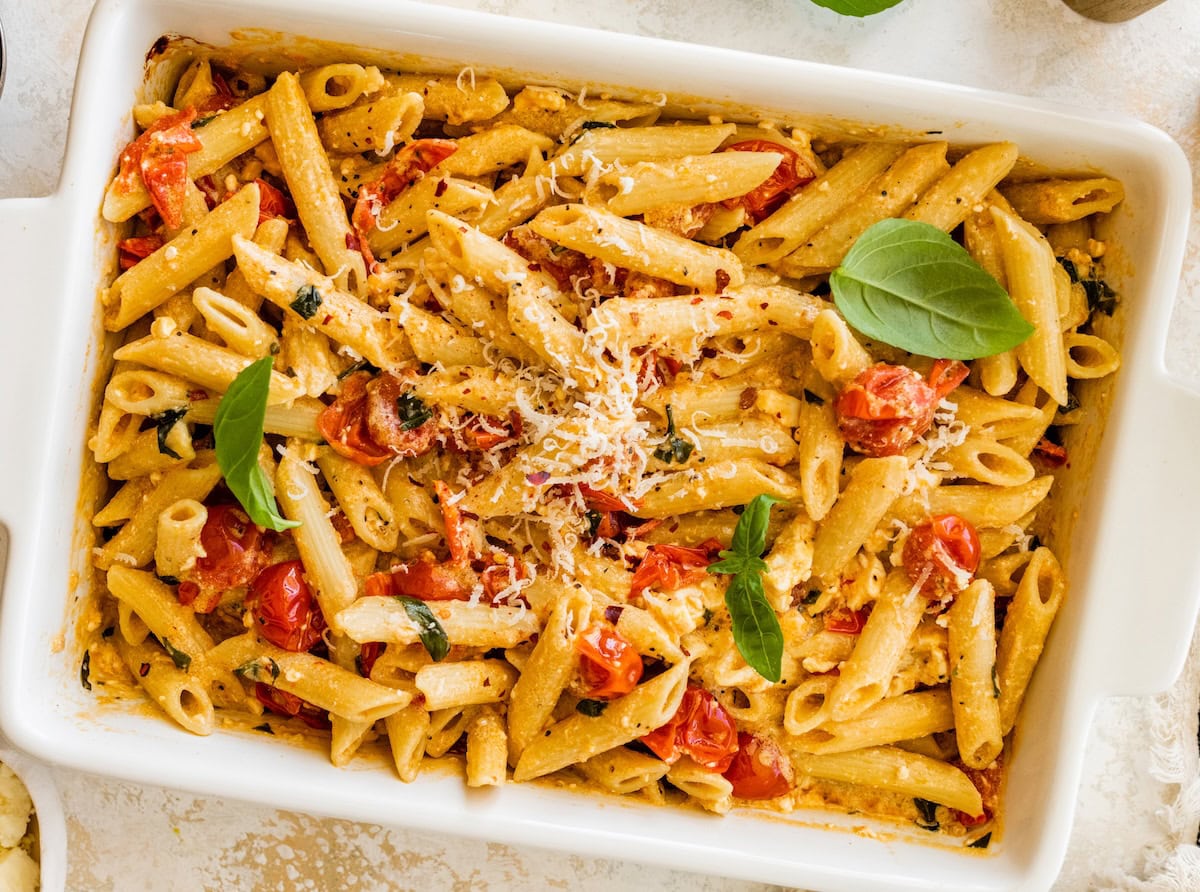 Baked feta pasta in a white baking dish topped with basil and grated parmesan.